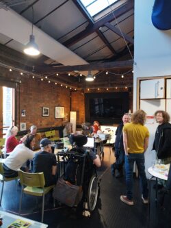 A group of people talking around tables in a room with lit with fairy lights. They are looking at laptops and materials