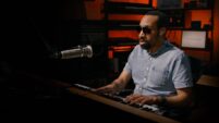 Andre Louis, a musician playing the keyboard in a dark studio setting.