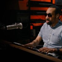 Andre Louis, a musician playing the keyboard in a dark studio setting.
